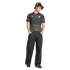 A man in a black Adidas Jamaica jersey with colorful patterns, matching bucket hat, and wide-leg dark jeans stands against a black background.