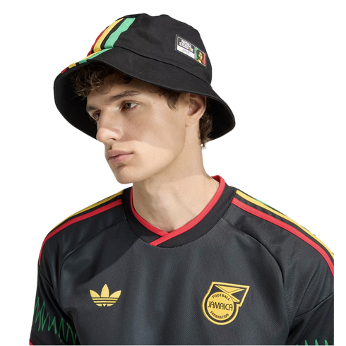 Young man in a black Adidas Jamaica soccer jersey and matching bucket hat with green, yellow, and red accents, posed against a solid black background.