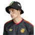 Young man in a black Adidas Jamaica soccer jersey and matching bucket hat with green, yellow, and red accents, posed against a solid black background.