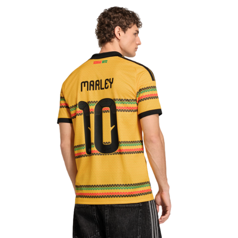 Rear view of a man in a yellow Jamaica "Marley 10" jersey with green, red, and black patterned stripes against a black background.