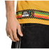 Close-up of a yellow jersey with a Bob Marley "Football is Freedom" patch and knit-patterned stripes, worn with black striped denim. A silver ring is visible on the person's hand.