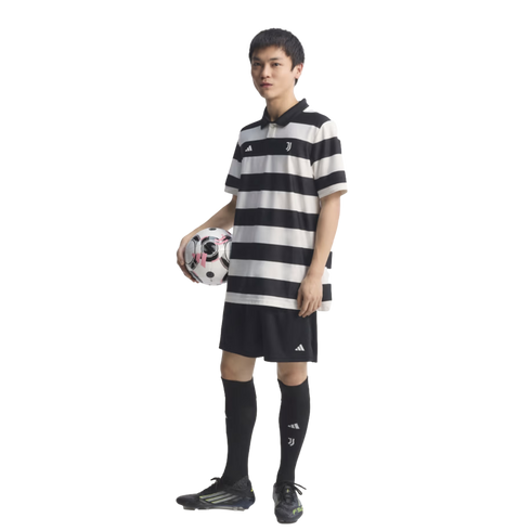A man in a black and white striped Juventus soccer jersey and black shorts holds a soccer ball under his arm against a black background.