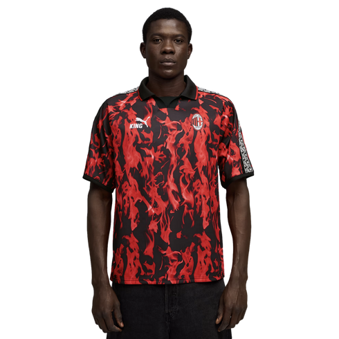 Man in a red and black flame-patterned AC Milan soccer jersey with a black collar, standing against a black background.