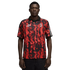 Man in a red and black flame-patterned AC Milan soccer jersey with a black collar, standing against a black background.