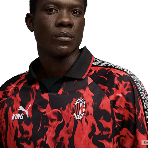 A man wears an AC Milan x Puma King football jersey featuring a red and black flame design, the club crest, and patterned shoulder trim.