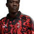 A man wears an AC Milan x Puma King football jersey featuring a red and black flame design, the club crest, and patterned shoulder trim.