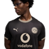 A man wearing glasses and a black Puma football jersey featuring the Borussia Dortmund (BVB) crest and a Vodafone sponsor logo, set against a black background.