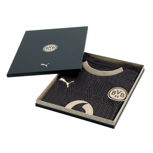 A black Borussia Dortmund soccer jersey with gold Puma and BVB logos, inside an open black presentation box.