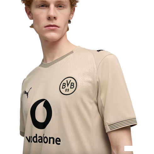 A young man with red hair wearing a tan BVB 09 soccer jersey by Puma with a black Vodafone logo, set against a plain black background.