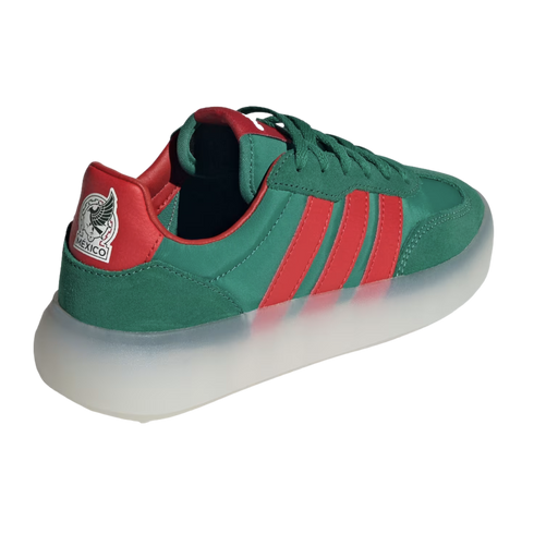 A three-quarter rear view of a green Adidas sneaker featuring red stripes and a thick, translucent white platform sole. The red heel tab is adorned with the Mexico national football team's eagle crest and the word "MÉXICO."