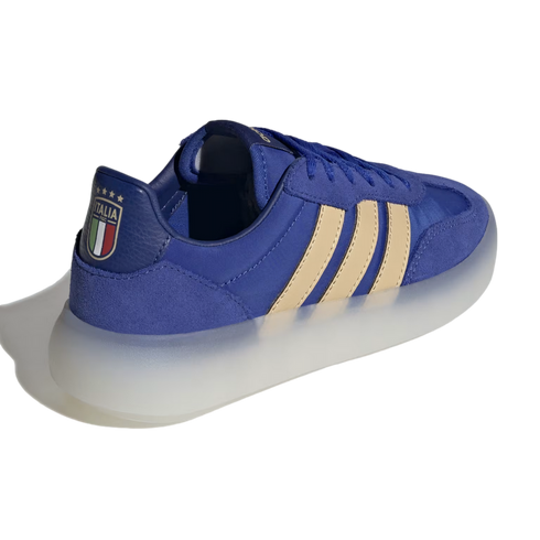 A blue suede and mesh sneaker with three cream-colored stripes and a thick, translucent white sole. The heel tab features the Italian national football team (FIGC) crest with four gold stars above it.