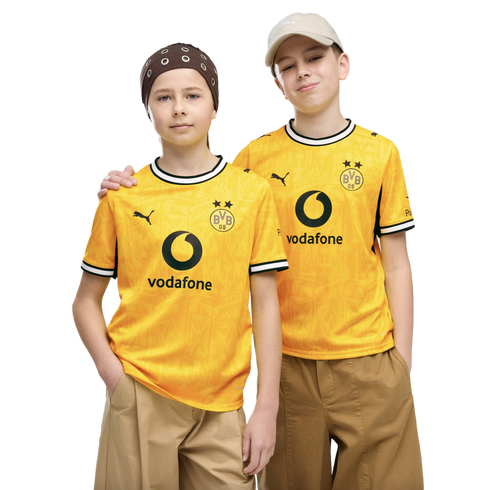 Two young people pose side-by-side in matching yellow Borussia Dortmund soccer jerseys against a black background. One wears a brown bandana and the other a beige baseball cap.
