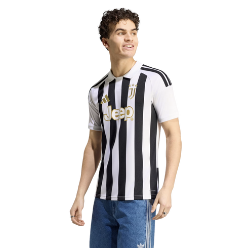 A smiling man wearing a Juventus black and white striped football jersey with gold accents and blue jeans, against a white background.