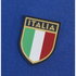 A close-up of a shield-shaped "ITALIA" patch on blue fabric, featuring gold text above vertical green, white, and red stripes.