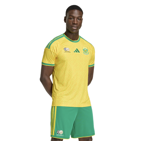 A man models the yellow and green Adidas South Africa national football team kit against a plain white background.
