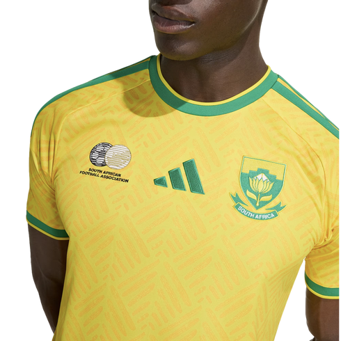 Close-up of a person wearing a yellow South Africa national football team jersey with green accents, featuring the Adidas logo and team crests.
