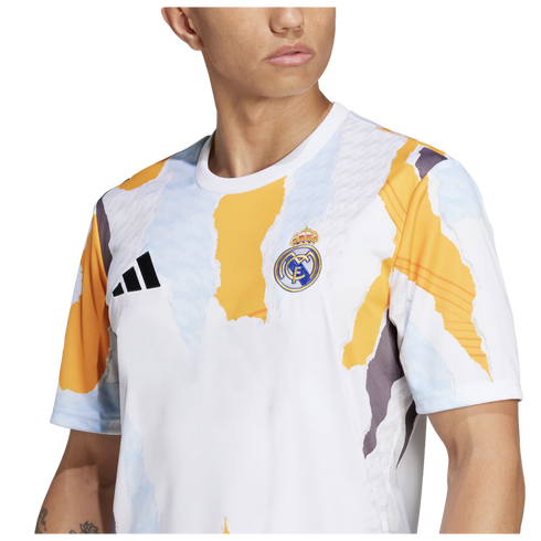 A person wearing an Adidas Real Madrid pre-match jersey featuring a white base with an abstract yellow, light blue, and grey torn-paper pattern. The Real Madrid club crest is visible on the left chest and the black Adidas logo on the right.