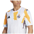 A person wearing an Adidas Real Madrid pre-match jersey featuring a white base with an abstract yellow, light blue, and grey torn-paper pattern. The Real Madrid club crest is visible on the left chest and the black Adidas logo on the right.