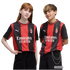 A red-haired girl and a blonde boy pose side-by-side in matching red and black AC Milan football jerseys against a plain white background.