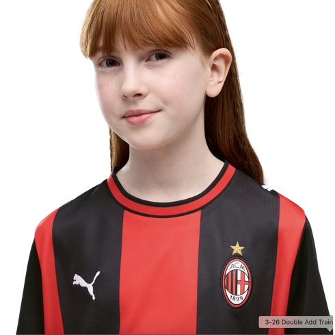 A young girl with long red hair and freckles wears a red and black striped AC Milan football jersey.
