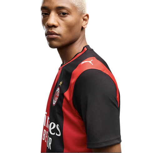 A blonde man wearing a red and black AC Milan soccer jersey with a Puma logo, looking at the camera against a white background.