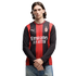 A man with mid-length dark hair wearing an AC Milan long-sleeved soccer jersey and blue jeans, standing against a plain white background.