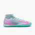 Light blue Nike indoor soccer shoe with a pink swoosh, pink heel graphics, and a bright teal sole. Features a mid-cut collar and "AIR ZOOM" technology.